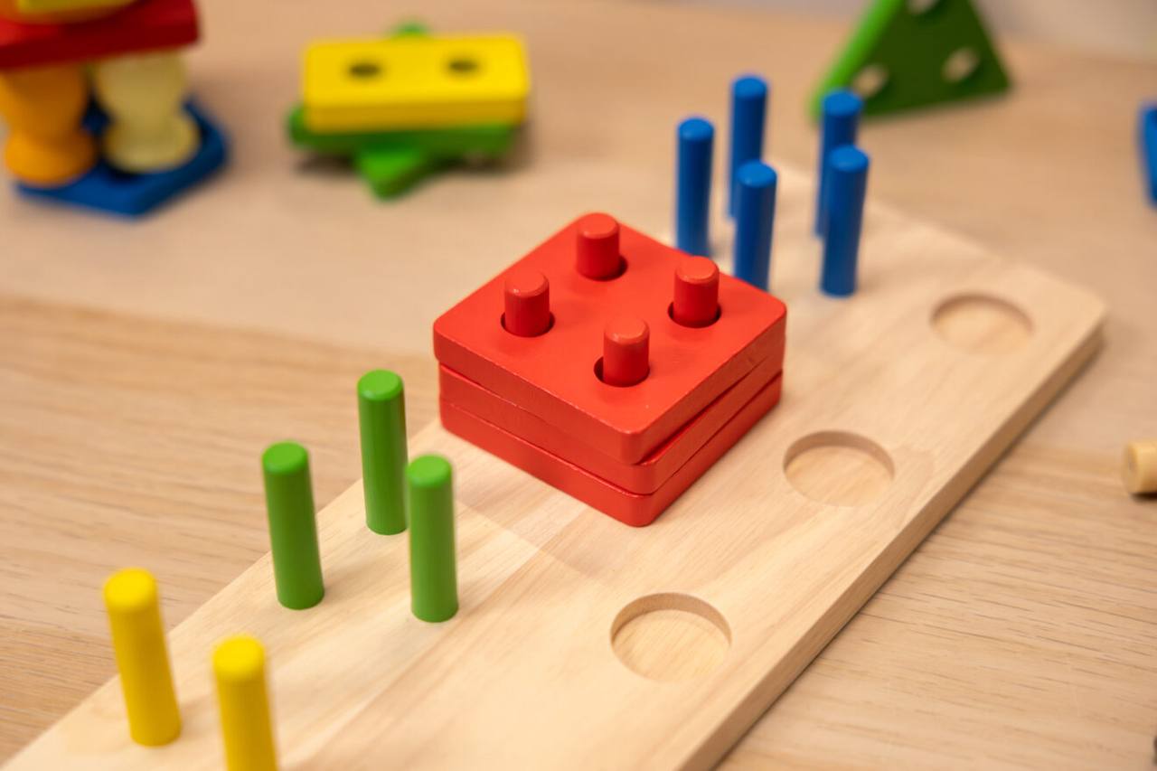 Kind sortiert bunte geometrische Formen beim Montessori Steckspiel